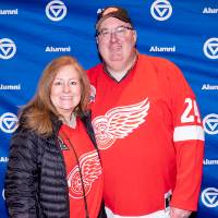 Couple wearing Red Wings jerseys posing for photo in front of GVSU backdrop